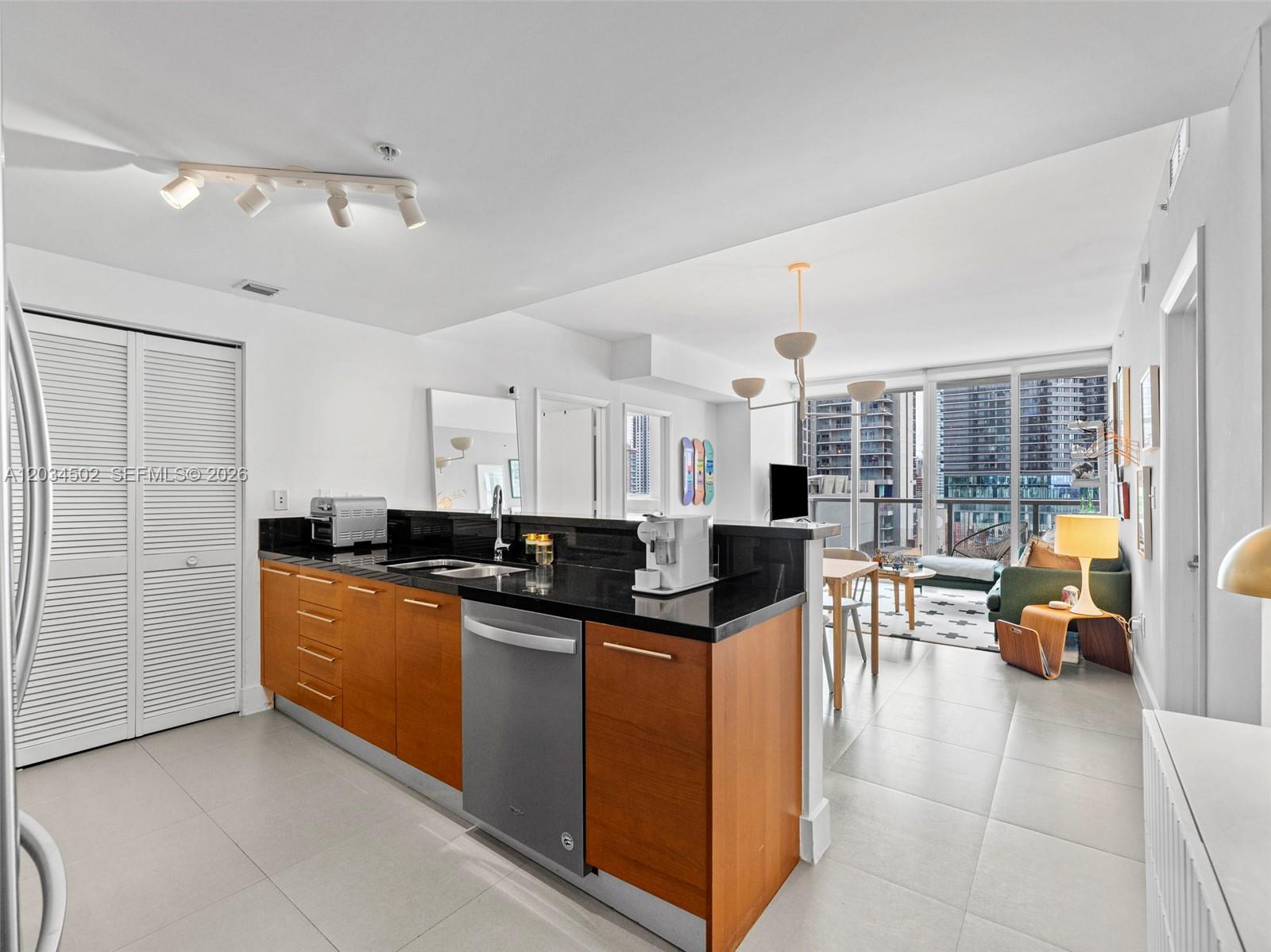 A kitchen with wood cabinets and black countertops opens into a living area with floor-to-ceiling windows — 253 NE 2nd St # 1801, Miami FL 33132, MIAMI, FL
