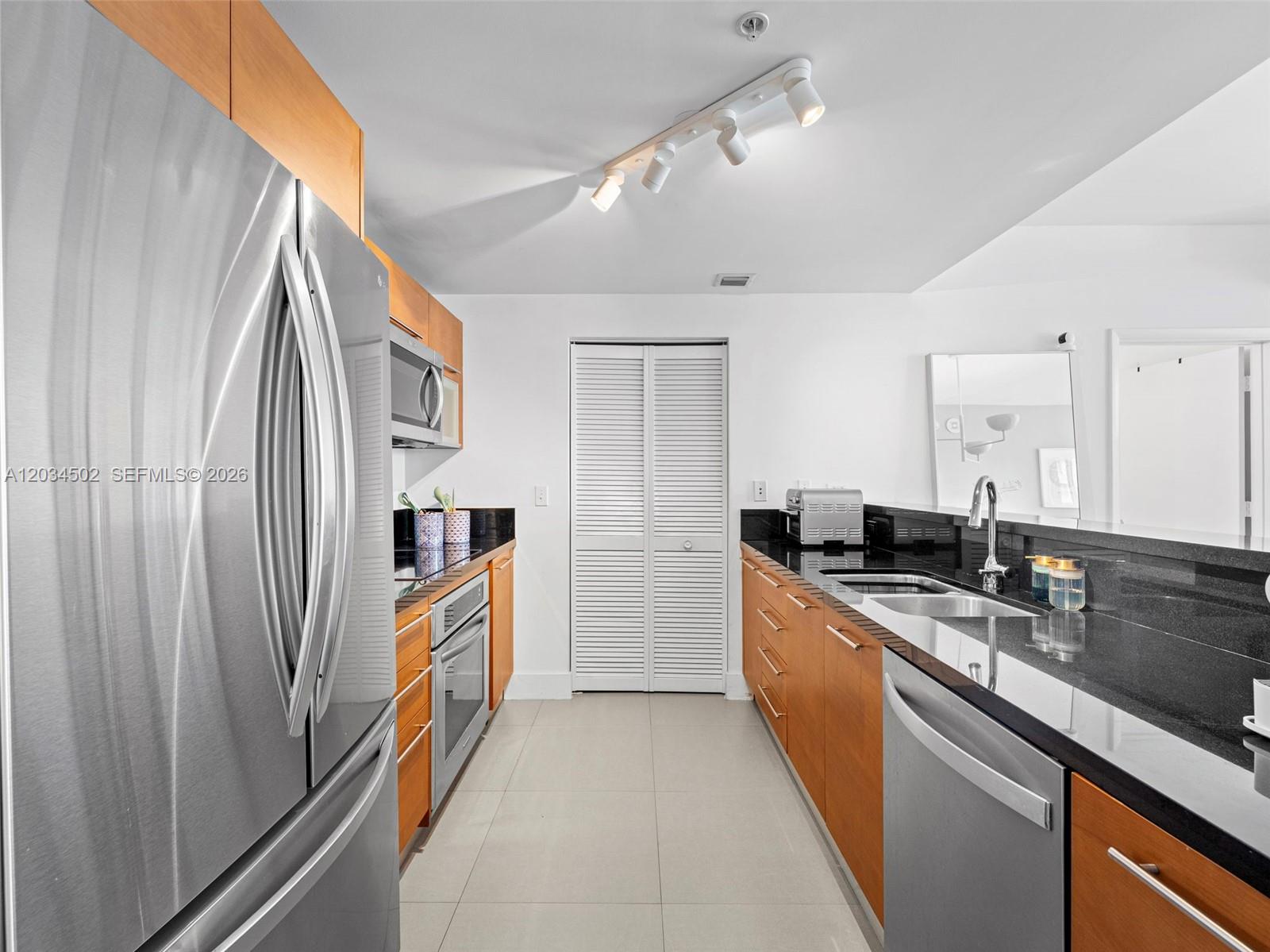 A galley kitchen features wood cabinets, black countertops, stainless steel appliances, and white tile flooring — 253 NE 2nd St # 1801, Miami FL 33132, MIAMI, FL