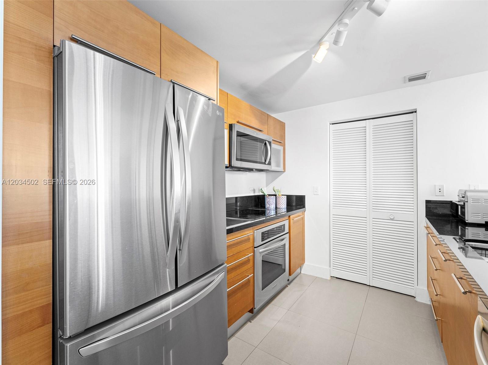 A kitchen features stainless steel appliances, wood cabinetry, and black countertops — 253 NE 2nd St # 1801, Miami FL 33132, MIAMI, FL