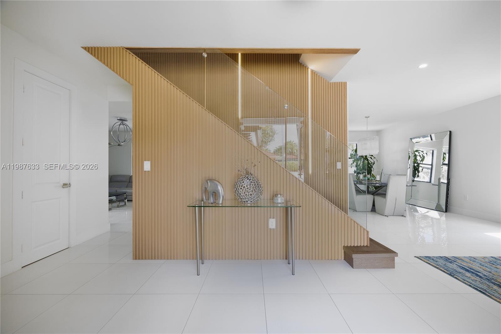 A modern entryway features a slatted wood staircase wall with a glass railing and console — 2981 SW 149th Ave, Miami FL 33185, MIAMI, FL