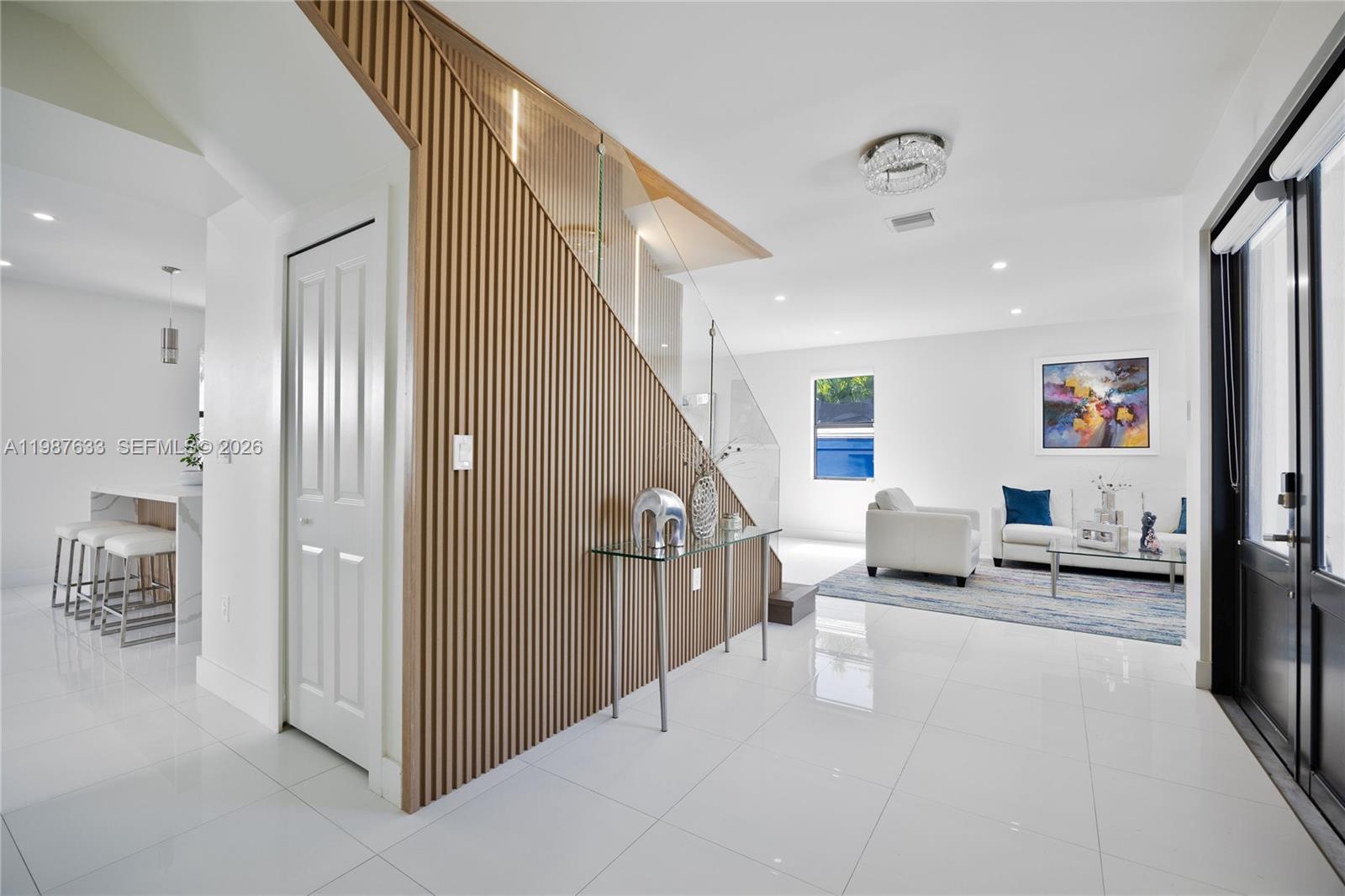 A modern living room features white tile floors, a slatted wood staircase wall, and glass railings — 2981 SW 149th Ave, Miami FL 33185, MIAMI, FL