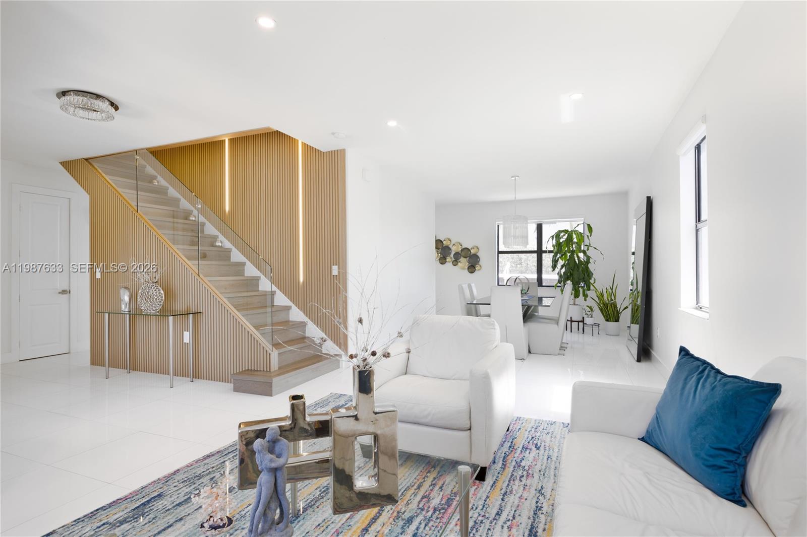 A modern living and dining area features a wood-slat staircase, white tile floors, and furniture — 2981 SW 149th Ave, Miami FL 33185, MIAMI, FL