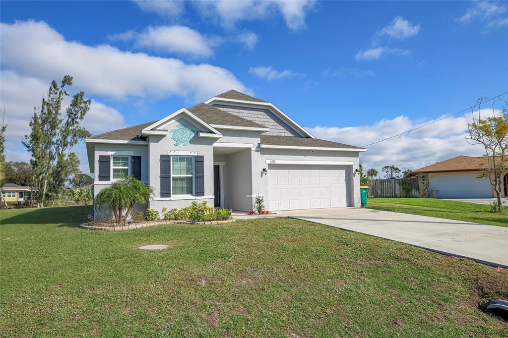 A single-story house with a two-car garage, light gray stucco exterior, and a turtle wall decoration — 3215 BROOKLYN AVENUE, PORT CHARLOTTE, FL