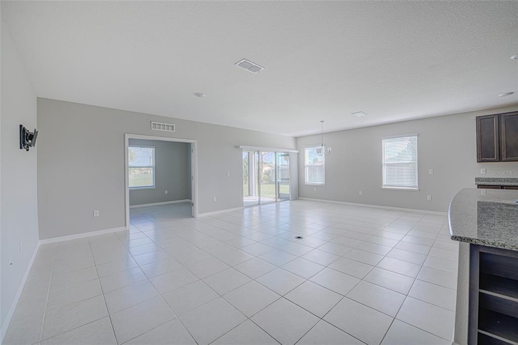 A spacious, open-concept living area features light-colored tile flooring, neutral walls, and sliding glass doors — 3215 BROOKLYN AVENUE, PORT CHARLOTTE, FL