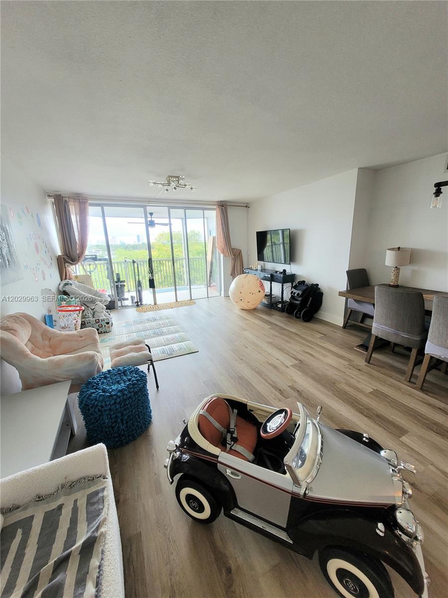 A living and dining area features light wood-look flooring, a balcony, and a toy car — 1780 NE 191st St # 2, Miami FL 33179, MIAMI, FL