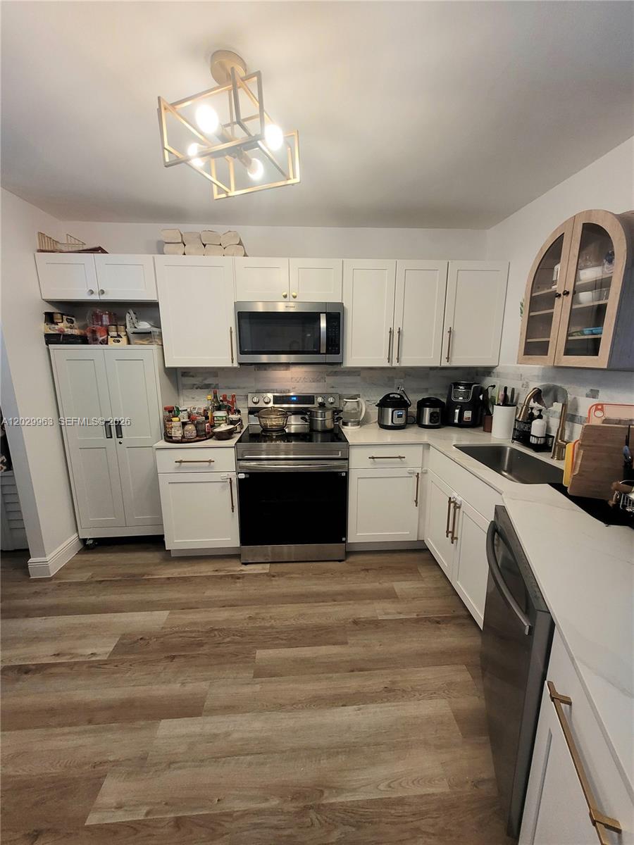 A kitchen features white cabinets, stainless steel appliances, a light fixture, and wood-look flooring — 1780 NE 191st St # 2, Miami FL 33179, MIAMI, FL