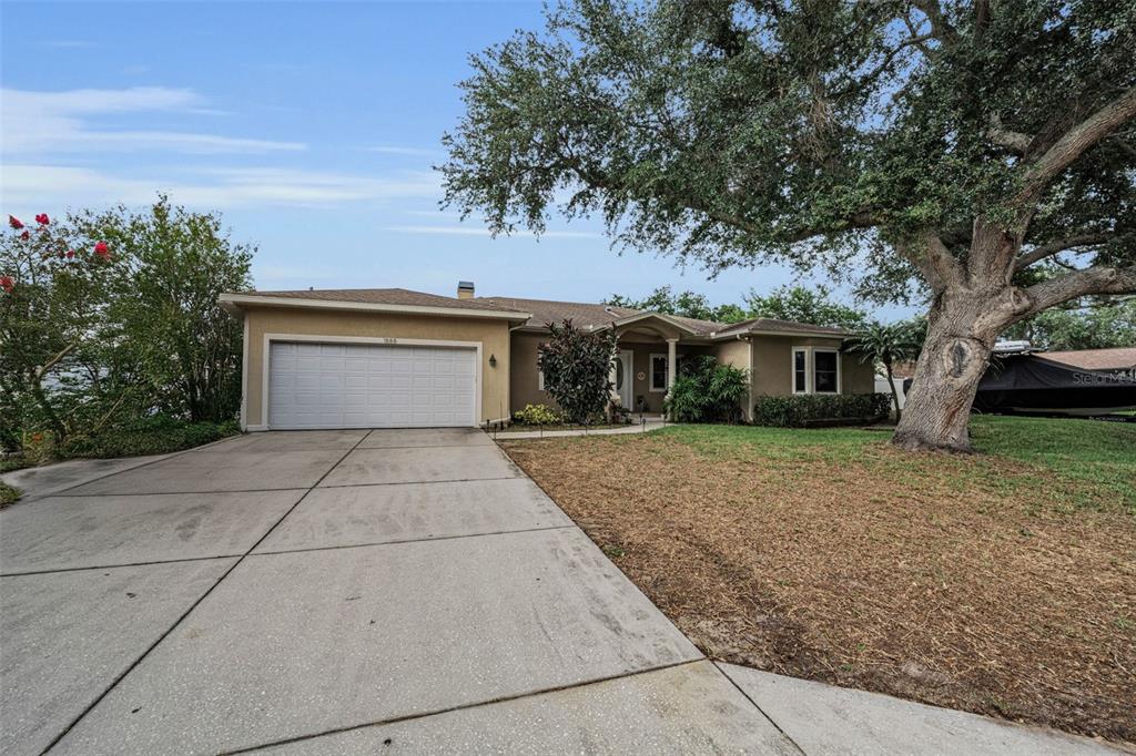 A single-story house with a two-car garage and a large tree in the front yard — 1888 BUGLE LANE, CLEARWATER, FL