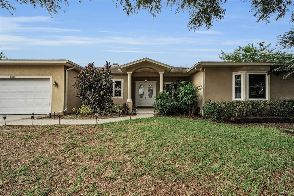 A single-story house with a two-car garage and a large tree in the front yard — 1888 BUGLE LANE, CLEARWATER, FL