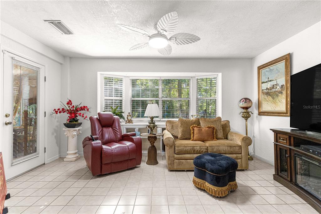 A living room features tile flooring, a ceiling fan, a bay window, and assorted furniture — 11465 SW 75TH TERRACE ROAD, OCALA, FL