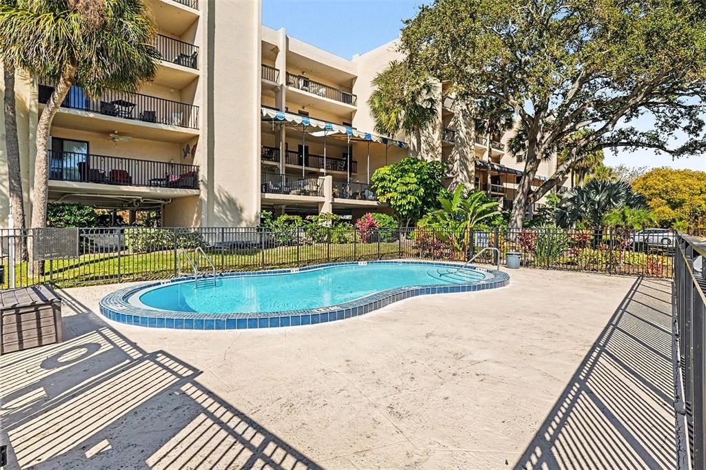 An outdoor swimming pool sits on a concrete patio in front of a multi-story building — 303 TARPON POINT, TARPON SPRINGS, FL