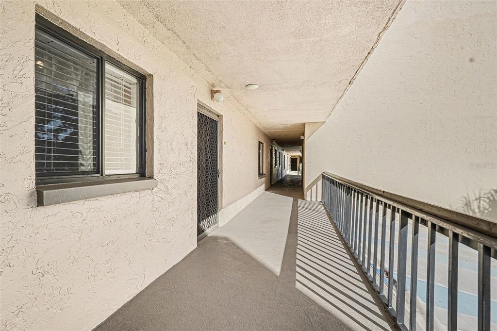 An outdoor apartment building walkway with a metal railing, stucco walls, and a screen door — 303 TARPON POINT, TARPON SPRINGS, FL