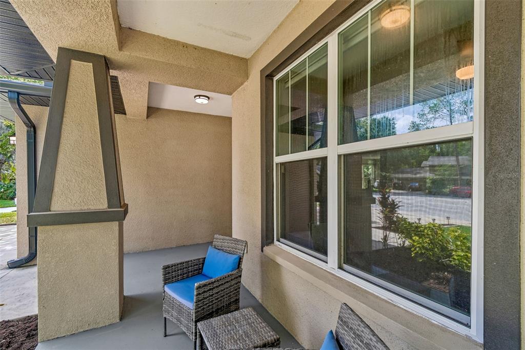 A covered porch features a stucco wall, a large window, and two wicker chairs — 21620 TEAL COURT, LUTZ, FL