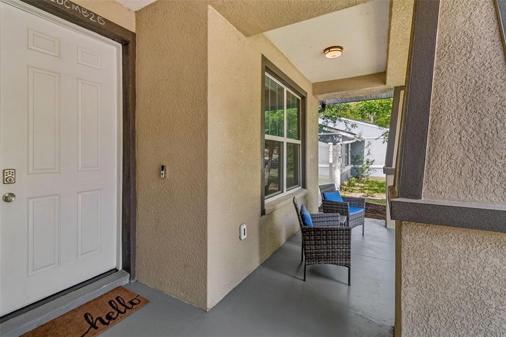 A covered front porch features a white door, two wicker chairs, and a welcome mat — 21620 TEAL COURT, LUTZ, FL