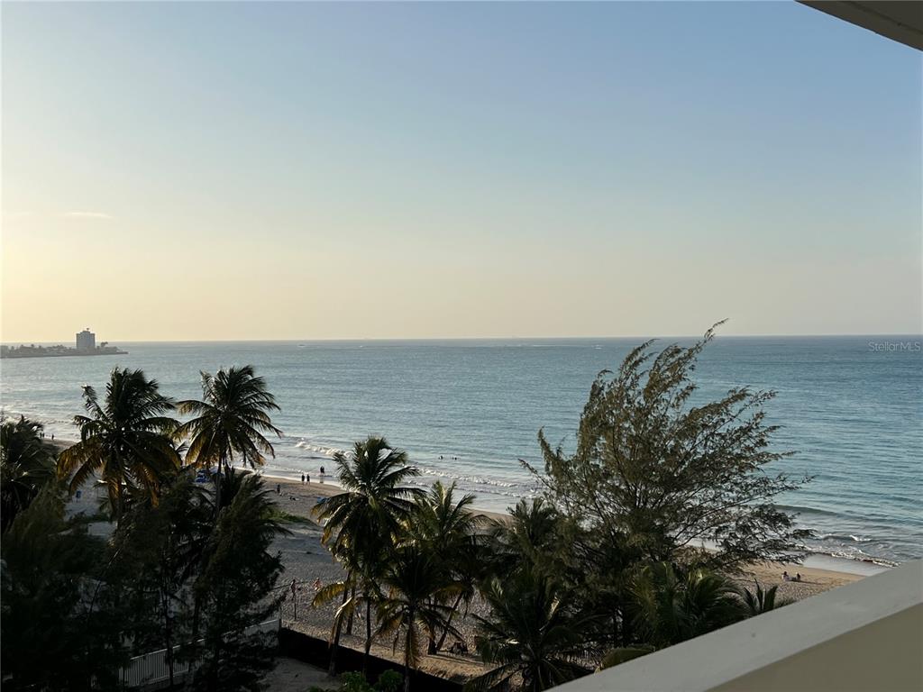 A high-angle view of a sandy beach and ocean from a balcony with palm trees — 4939 ISLA VERDE AVENUE UNIT 801, CAROLINA, PR