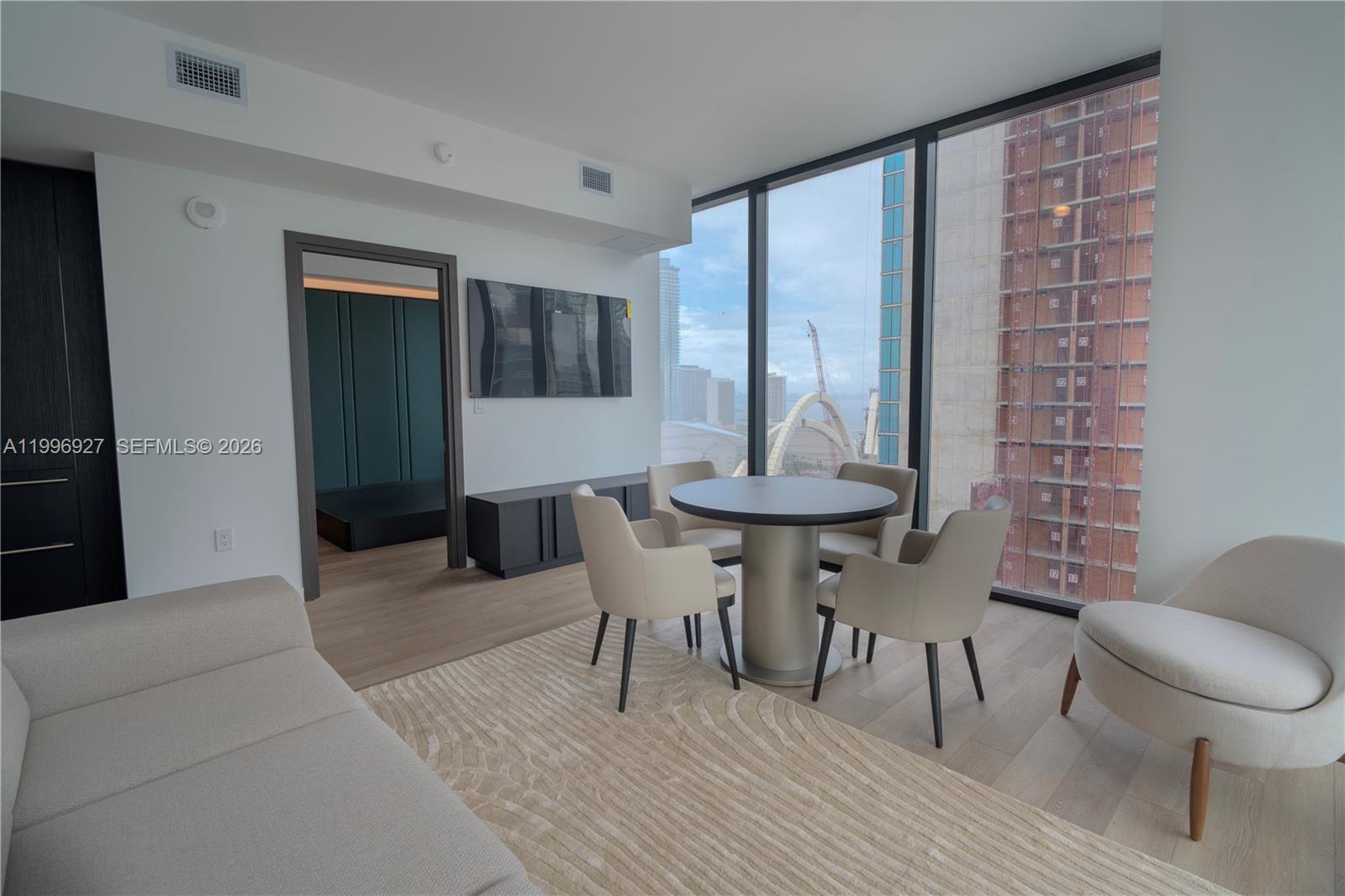 A modern living and dining area features floor-to-ceiling windows overlooking a city construction site — 20 NE 11th st # 2308, Miami FL 33132, MIAMI, FL