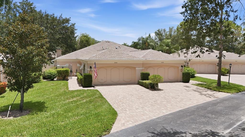 A single-story duplex with beige stucco walls, arched garage doors, and a paved driveway — 5435 CHANTECLAIRE UNIT 69, SARASOTA, FL