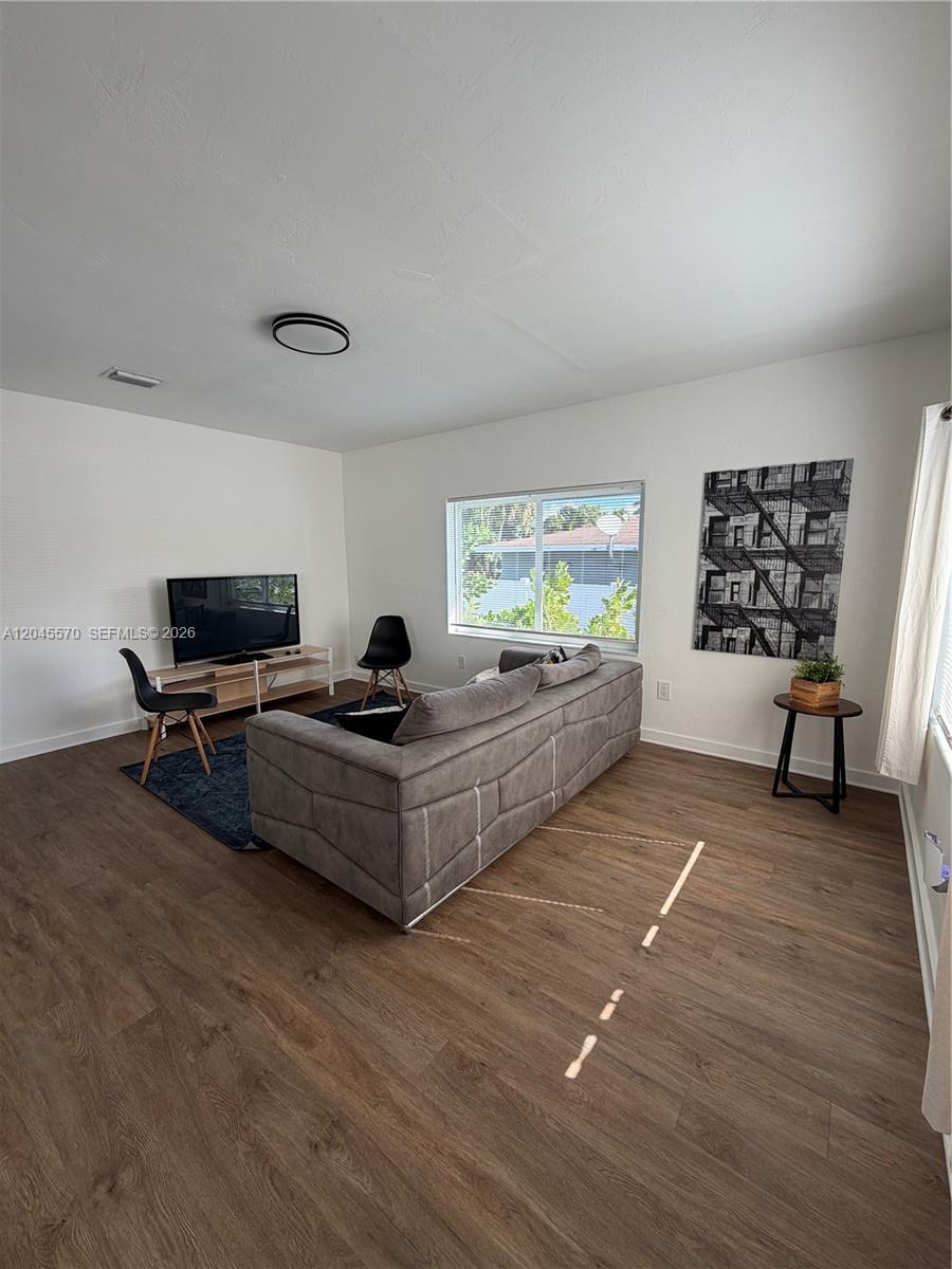 A living room features wood-look flooring, a gray sofa, a television, and a window — 1215 NE 109th St # 1215, Miami FL 33161, MIAMI, FL