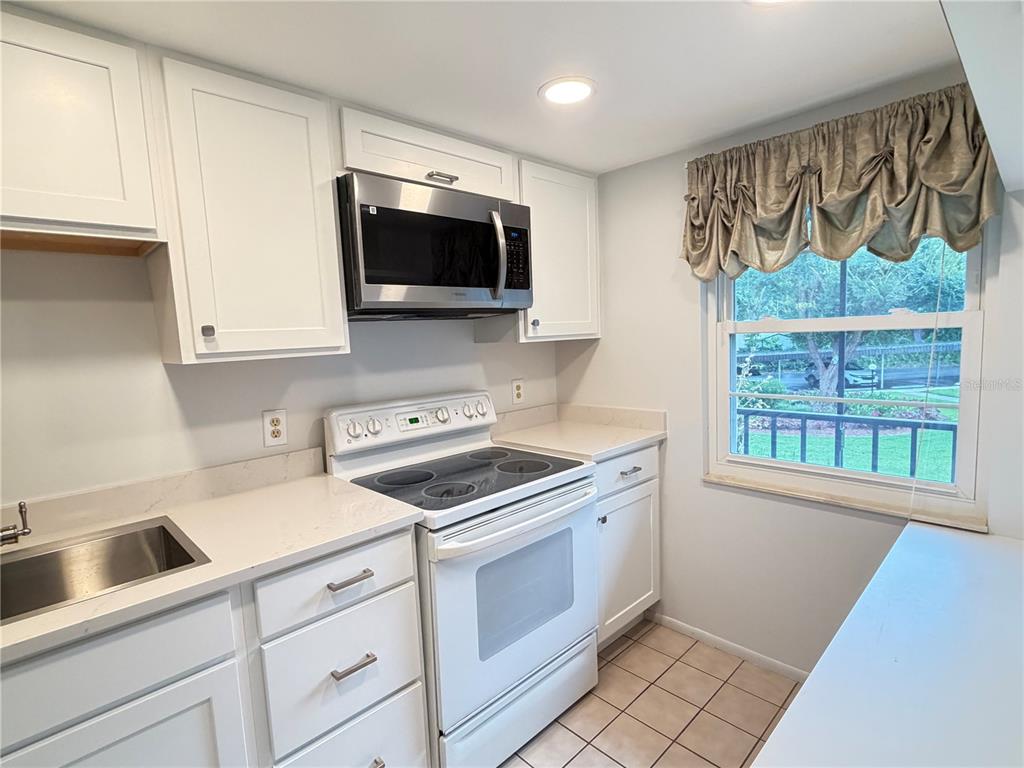 A kitchen with white cabinets, a stainless steel microwave, a white stove, and a window — 333 LAKE HOWARD DRIVE NW UNIT 211B, WINTER HAVEN, FL