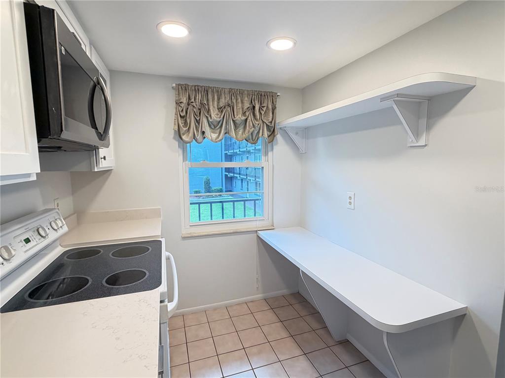 A kitchen features white counters, a glass-top stove, a window, and wall-mounted shelving — 333 LAKE HOWARD DRIVE NW UNIT 211B, WINTER HAVEN, FL