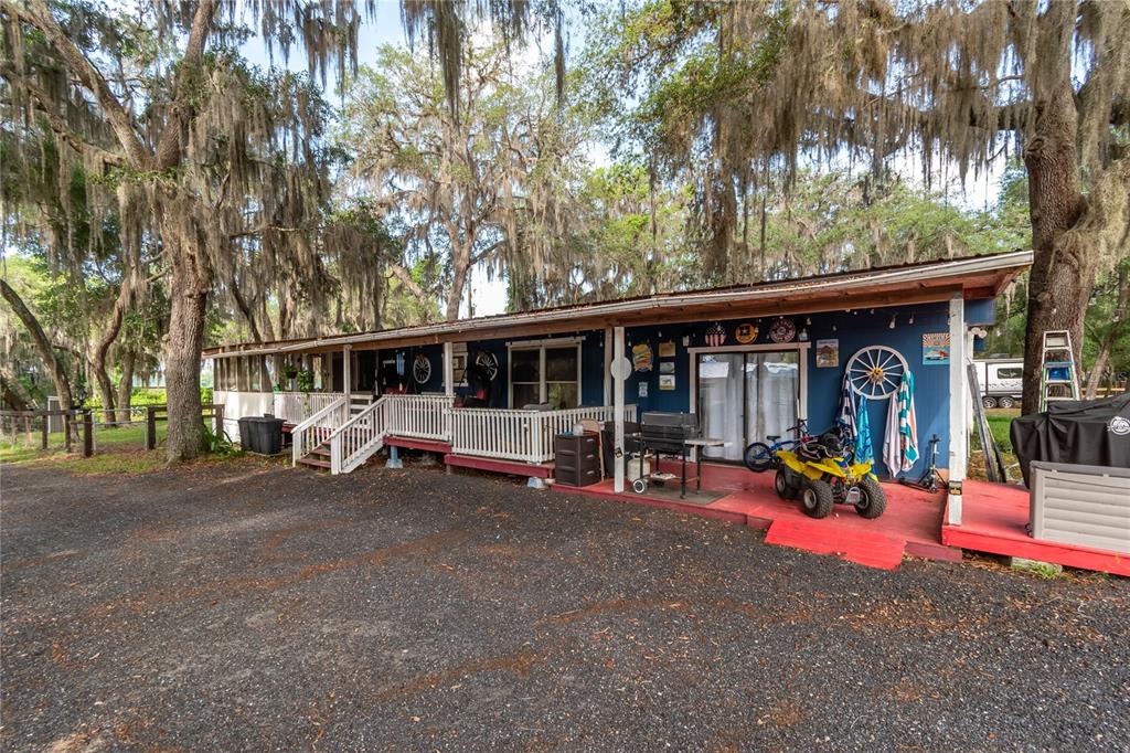 A blue mobile home with a covered porch sits on a gravel lot under trees — 134 FAYE STREET, HAWTHORNE, FL
