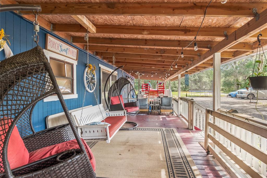 A covered wooden porch features hanging wicker chairs, a white bench, and string lights — 134 FAYE STREET, HAWTHORNE, FL