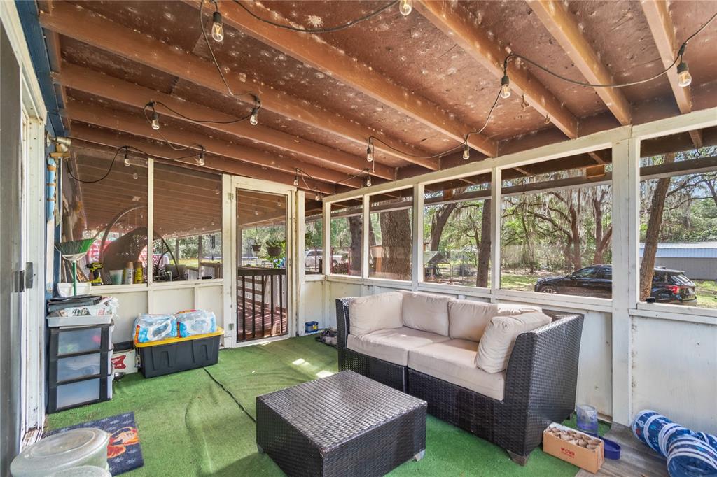 A screened-in porch features a wicker sofa, coffee table, green carpet, and exposed wood ceiling — 134 FAYE STREET, HAWTHORNE, FL