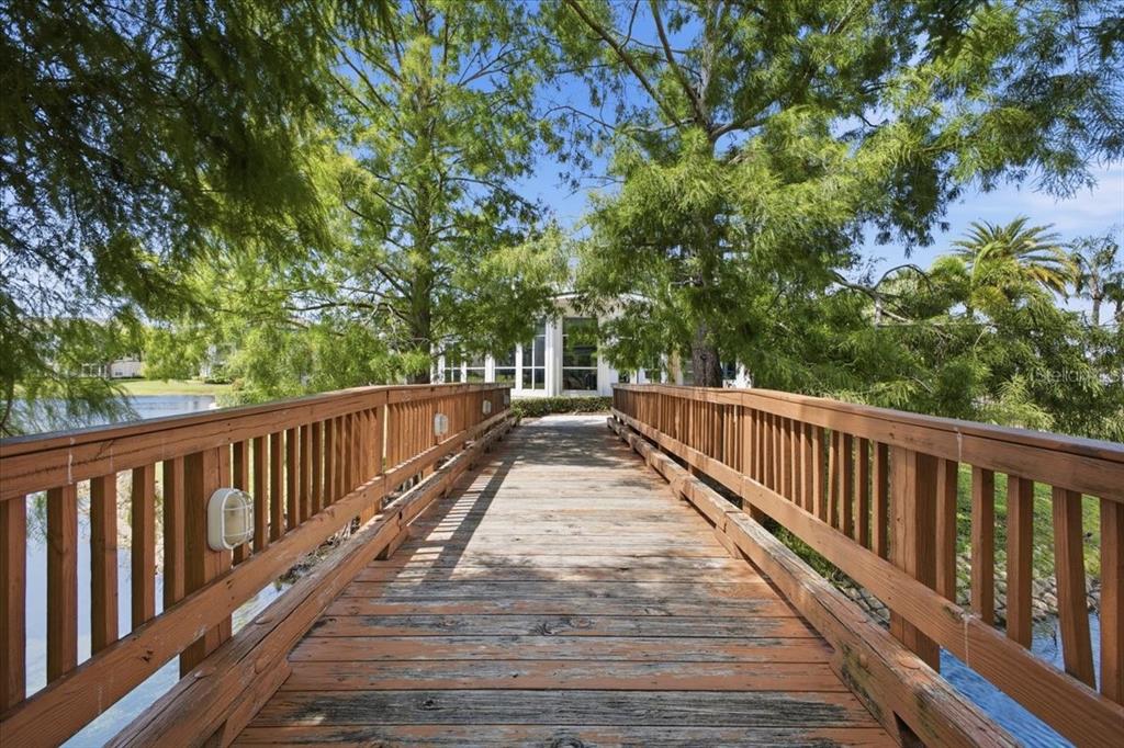 A wooden footbridge leads toward a white building surrounded by trees and a pond — 4802 51ST STREET W UNIT 903, BRADENTON, FL
