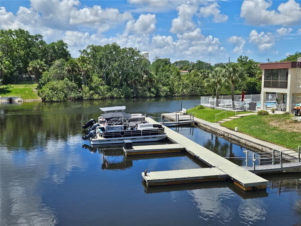 A pontoon boat is docked at a wooden pier on a calm canal near a house — 5640 FERGUSON COURT UNIT 2208, NEW PORT RICHEY, FL
