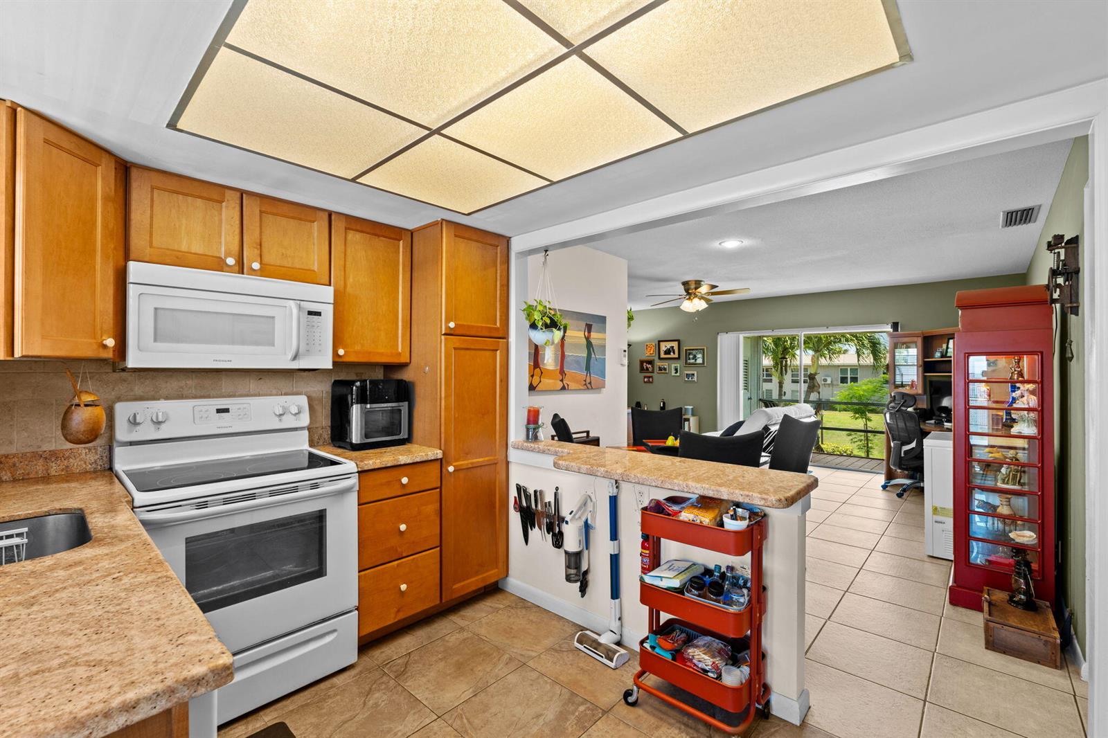A kitchen with wood cabinets, white appliances, and a breakfast bar overlooking a living area — 312 NE 17th Avenue # 203, Boynton Beach FL 33435, BOYNTON BEACH, FL