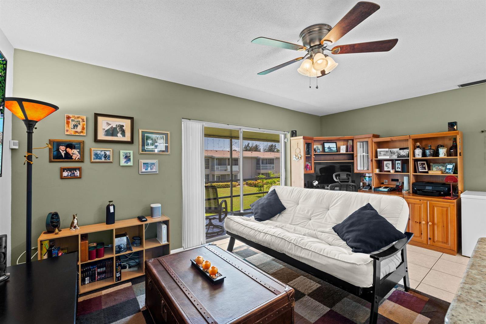 A living room features a futon, wooden shelving, a trunk coffee table, and sliding glass doors — 312 NE 17th Avenue # 203, Boynton Beach FL 33435, BOYNTON BEACH, FL