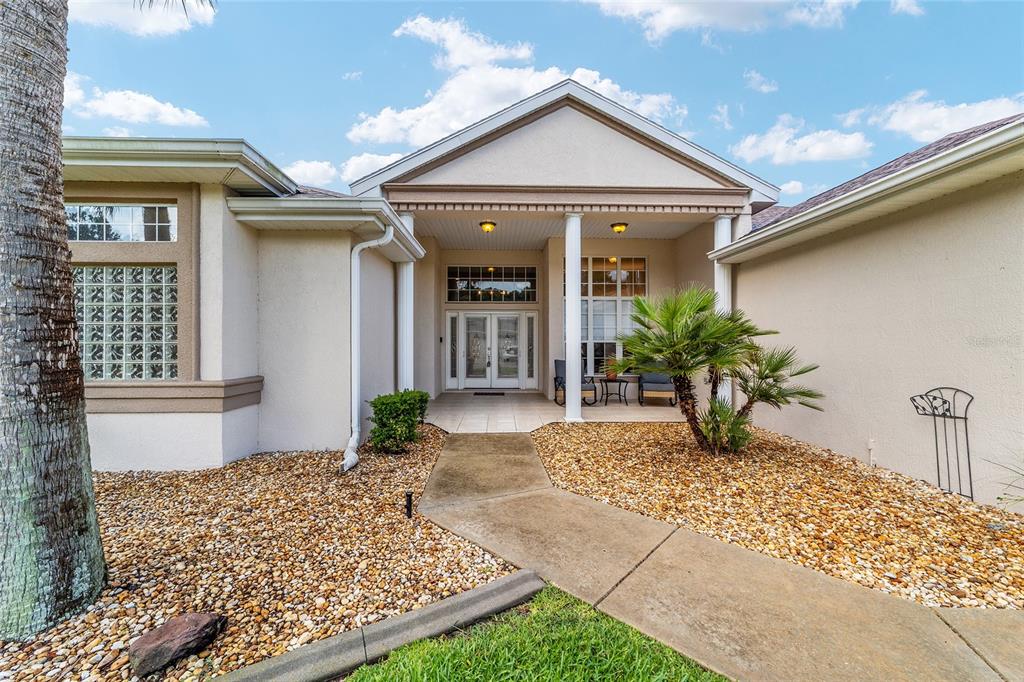 The exterior view shows a beige house with a covered entryway, palm tree, and gravel — 6577 SW 111TH LOOP, OCALA, FL
