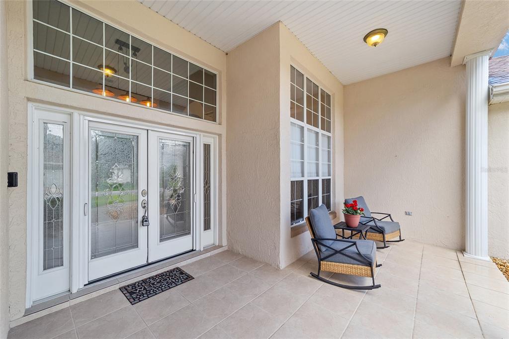 A covered front porch features tiled flooring, double glass doors, and two rocking chairs — 6577 SW 111TH LOOP, OCALA, FL