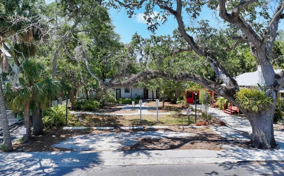 A gravel parking area sits in front of a building shaded by large oak trees — 1930 ADAMS LANE, SARASOTA, FL