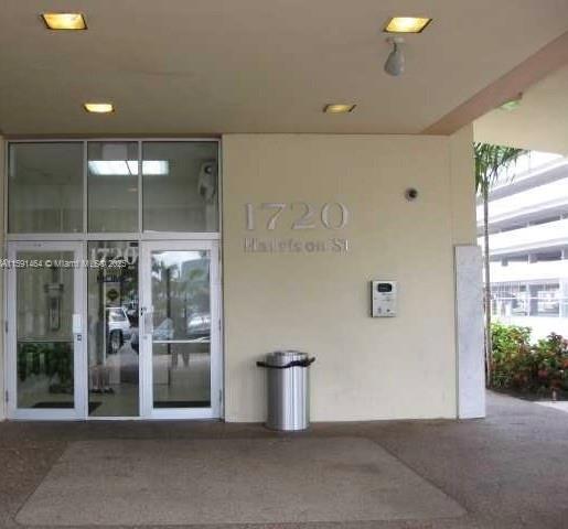 The exterior entrance of a building features glass doors, a trash receptacle, and building numbers — 1720 Harrison St # 8C, Hollywood FL 33020, HOLLYWOOD, FL