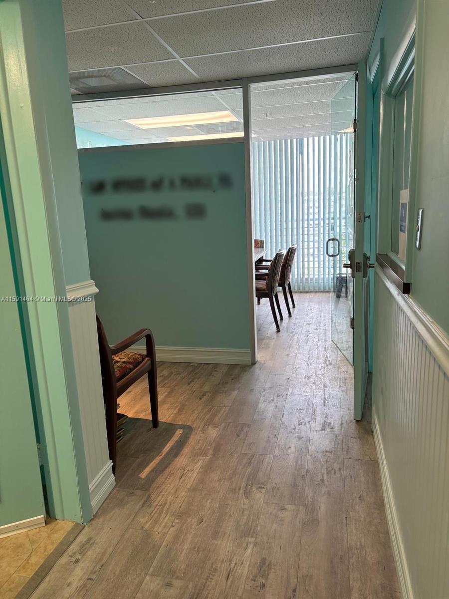 A view through an open doorway into an office space with wood-look flooring and blinds — 1720 Harrison St # 8C, Hollywood FL 33020, HOLLYWOOD, FL