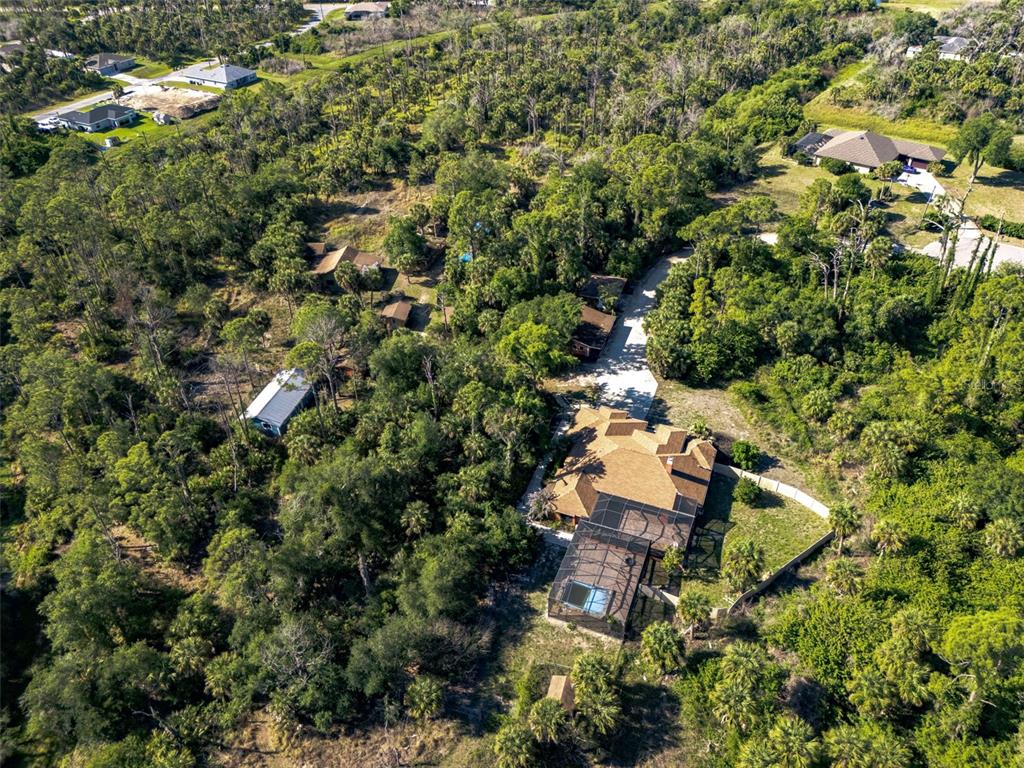 An aerial view shows a house with a pool cage surrounded by dense wooded vegetation — 3000 NARCISSUS TERRACE, NORTH PORT, FL