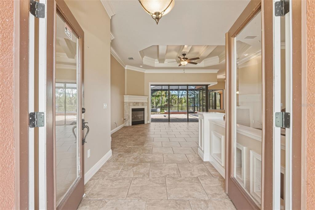 A view through double doors into a tiled living room with a fireplace and ceiling fan — 3000 NARCISSUS TERRACE, NORTH PORT, FL