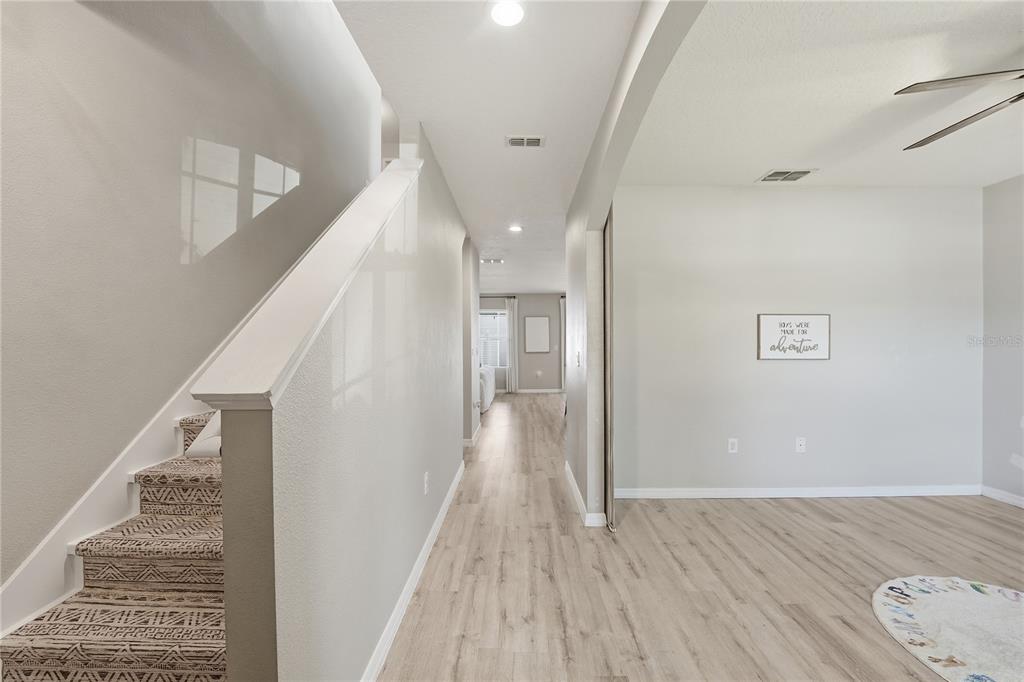 A hallway with wood-look flooring leads past a carpeted staircase to an open living area — 1895 GREEN DRAGON DRIVE, ST CLOUD, FL