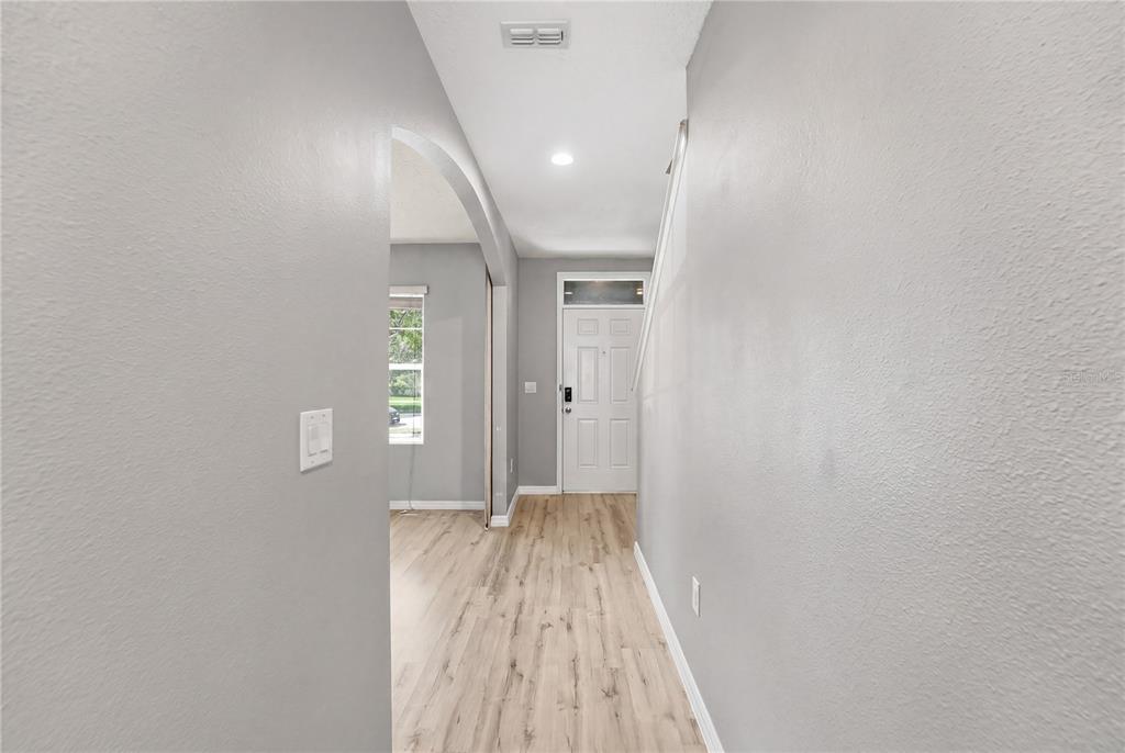 A hallway with light wood-look flooring leads to a white front door and an archway — 1895 GREEN DRAGON DRIVE, ST CLOUD, FL