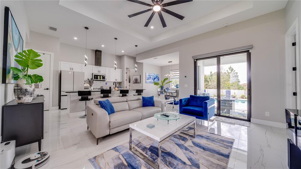 A modern open-concept living room and kitchen featuring white tile floors and blue accents — 4211 10TH STREET SW, LEHIGH ACRES, FL