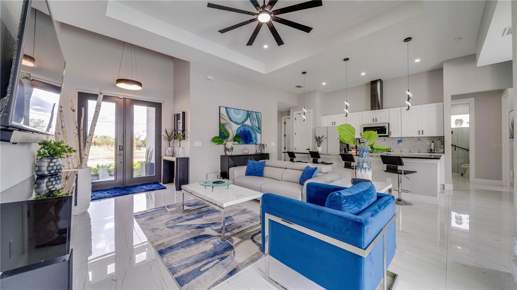 A modern open-concept living room and kitchen featuring white tile floors and blue accents — 4211 10TH STREET SW, LEHIGH ACRES, FL
