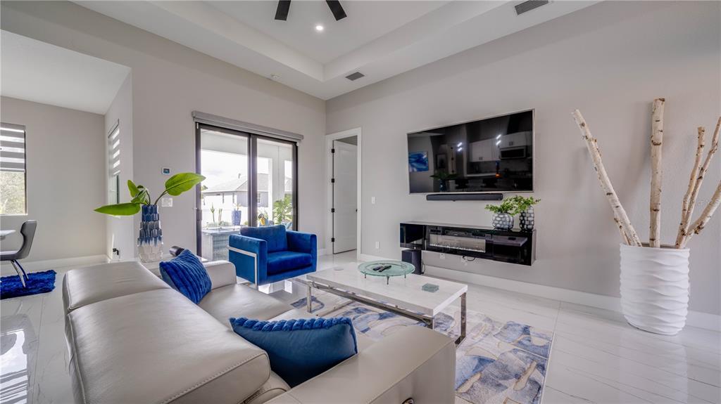 A modern living room features a white leather sofa, blue accent chairs, and a wall-mounted television — 4211 10TH STREET SW, LEHIGH ACRES, FL