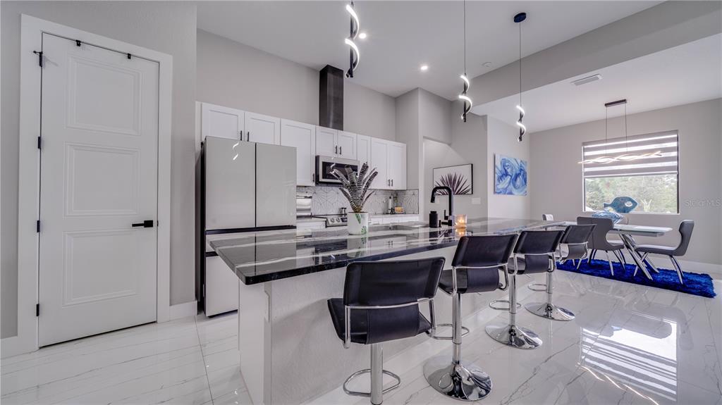A modern kitchen features a large black-and-white marble island, bar seating, and white cabinetry — 4211 10TH STREET SW, LEHIGH ACRES, FL