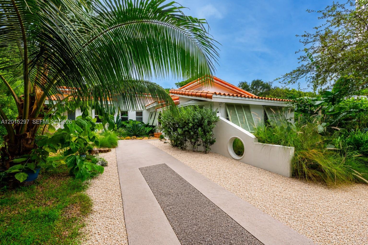 A concrete driveway leads to a white house with a terracotta tile roof and landscaping — 723 NE 112th St, Biscayne Park FL 33161, BISCAYNE PARK, FL
