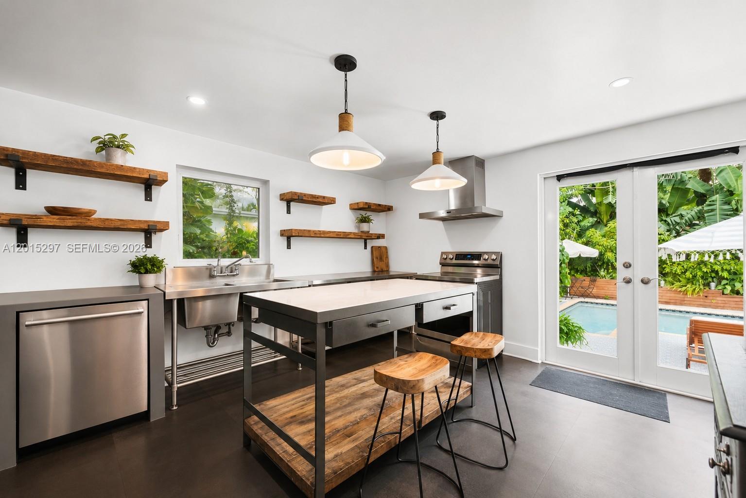 A modern kitchen features stainless steel appliances, wooden floating shelves, a central island, and pool views — 723 NE 112th St, Biscayne Park FL 33161, BISCAYNE PARK, FL