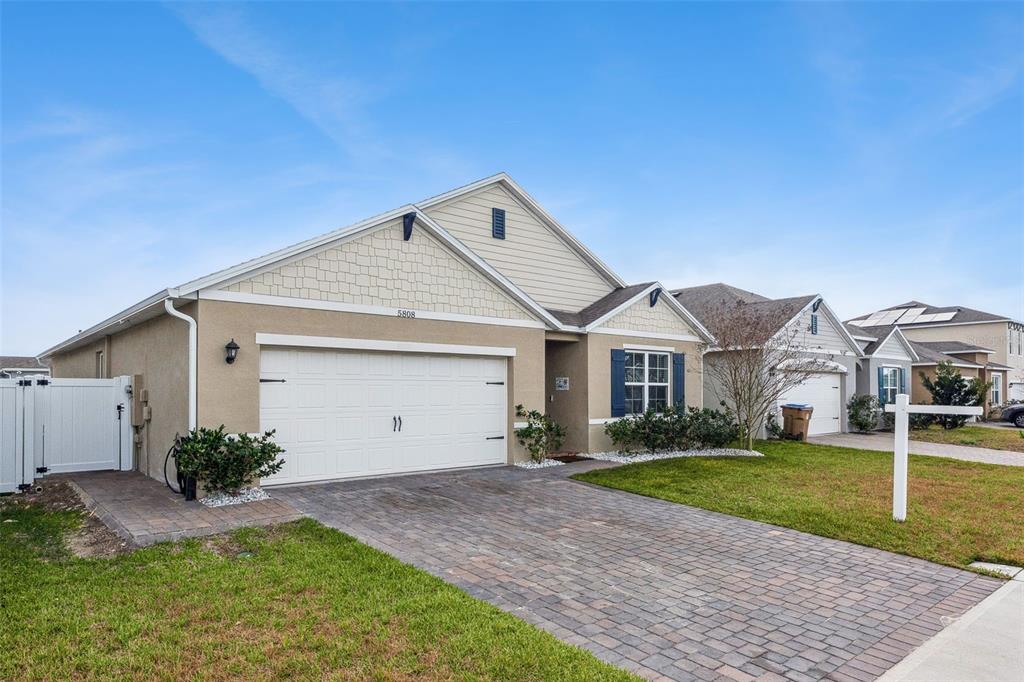 A single-story suburban house with a tan stucco exterior, shingle siding, and a paved driveway — 5808 ARBORETUM STREET, ST CLOUD, FL