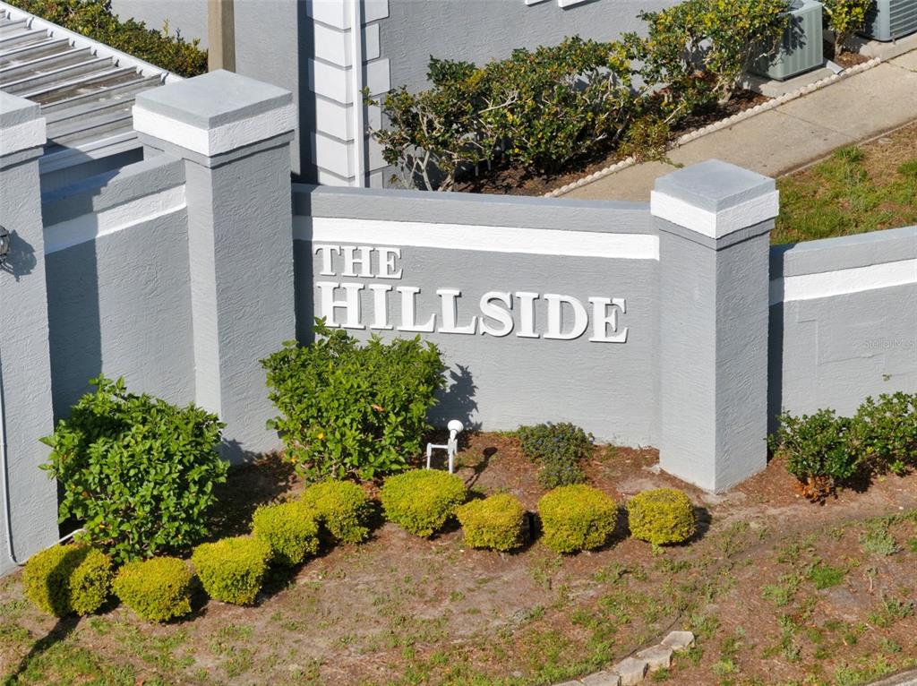 An exterior view of a gray stucco monument sign reading The Hillside with landscaping — 12133 SPARTAN WAY UNIT 204, HUDSON, FL