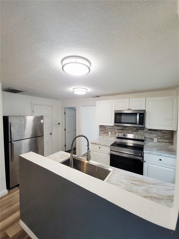 A kitchen features stainless steel appliances, white cabinets, a tiled backsplash, and a peninsula sink — 3532 38TH AVENUE N, ST PETERSBURG, FL