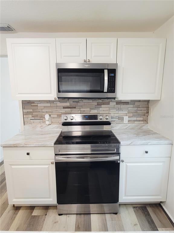 A kitchen features white cabinets, stainless steel appliances, a marble-look countertop, and a tiled backsplash — 3532 38TH AVENUE N, ST PETERSBURG, FL