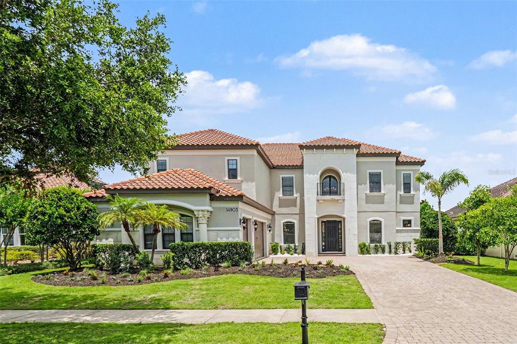 A two-story Mediterranean-style house with a tile roof, stone facade, and a paved driveway — 14903 OLD TOM MORRIS COURT, TAMPA, FL